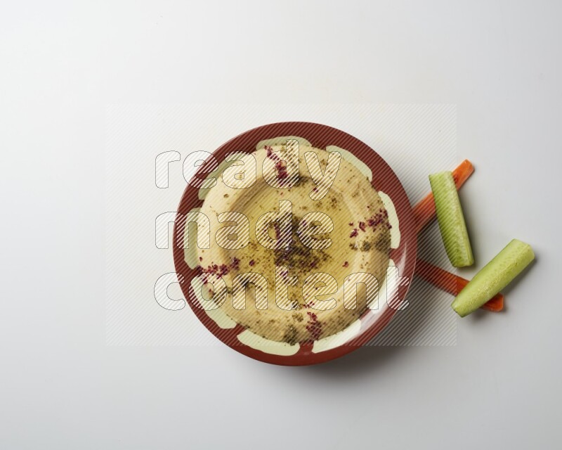 Hummus in a traditional plate garnished with zaatar & sumak on a white background