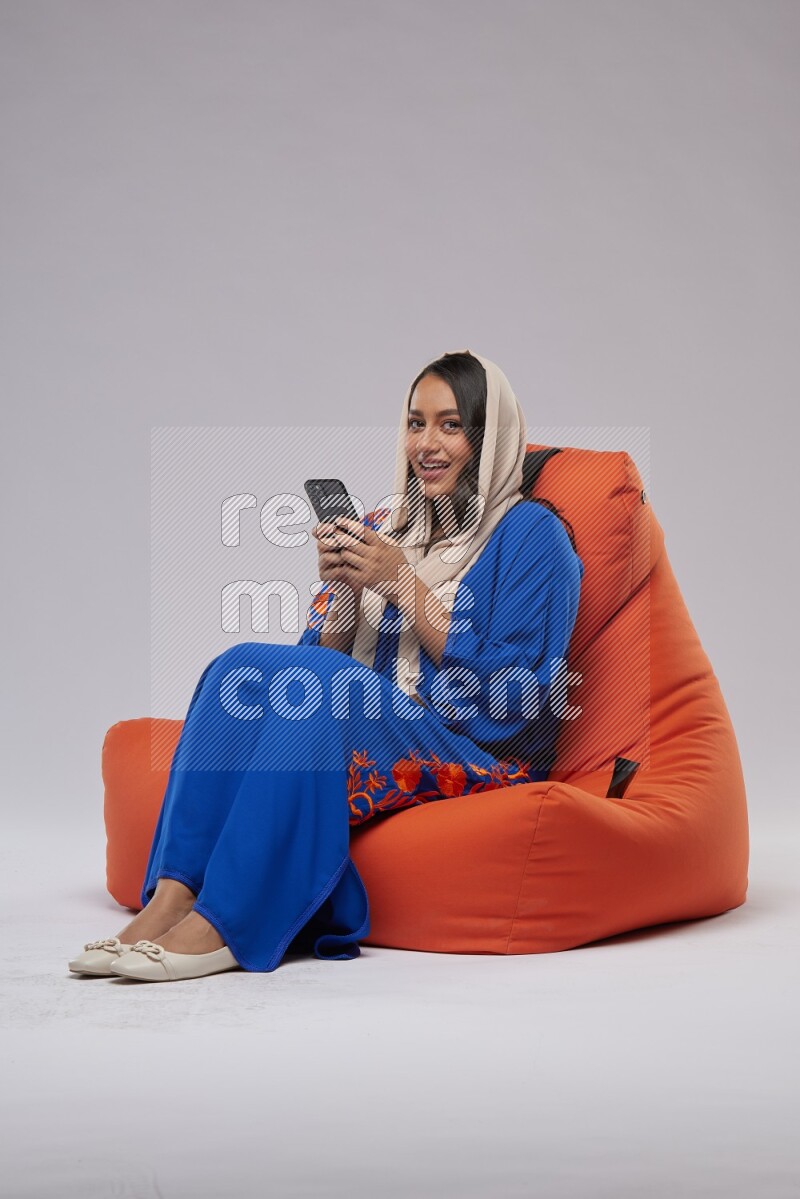 A Saudi woman sitting on an orange beanbag and texting on phone