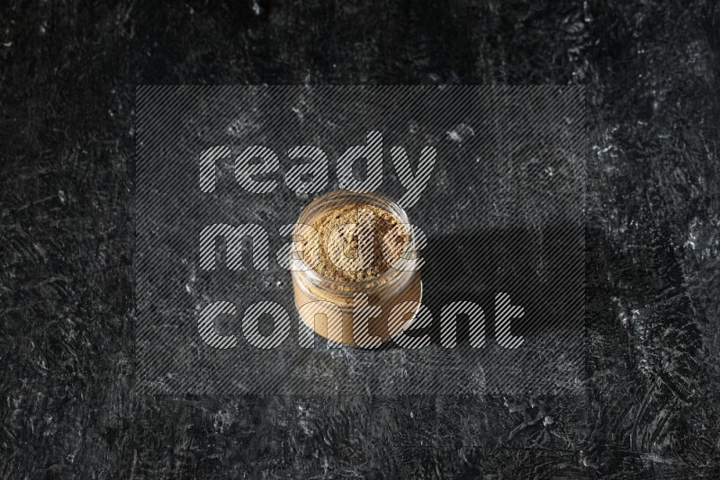 A glass jar full of allspice powder on a textured black flooring