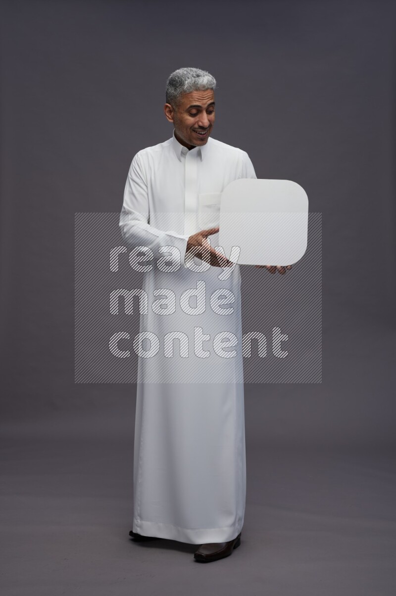 Saudi man wearing thob standing holding social media sign on gray background