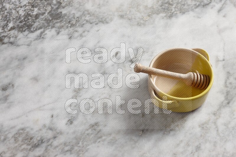 Multicolored pottery bowl with wooden honey dipper in it on grey marble background