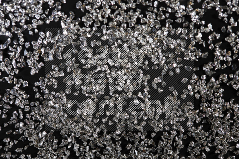 Silver shimmering fragments of glass scattered on a black background