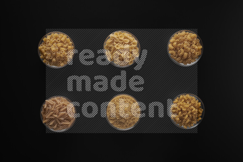 Different pasta types in 6 glass bowls on black background