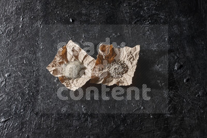 White pepper beads and powder in 2 crumpled paper on textured black flooring