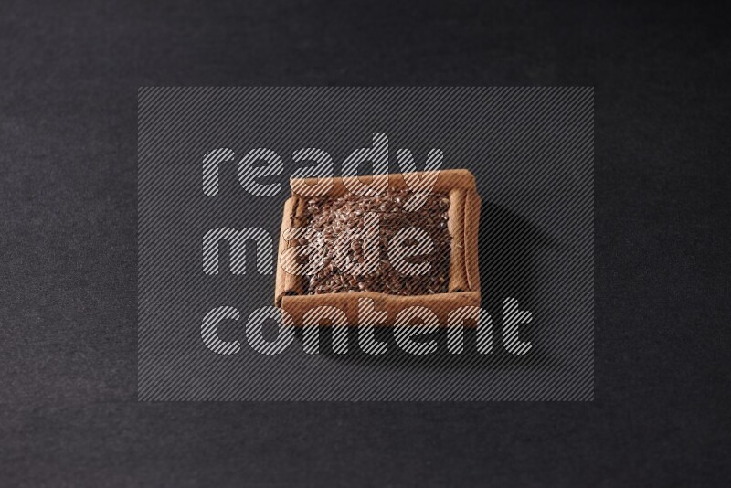 A single square of cinnamon sticks full of flaxseeds on black flooring