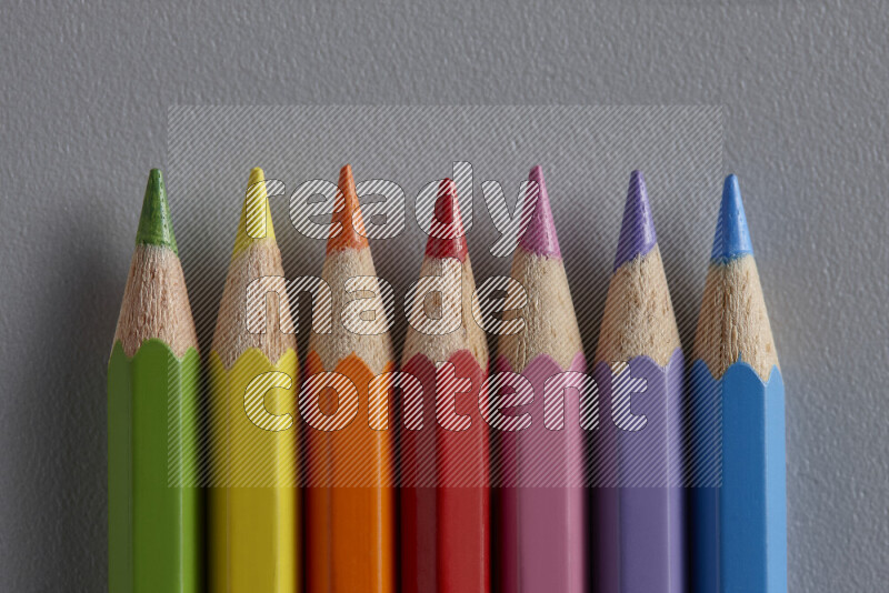 A collection of colored pencils arranged showcasing a gradient of different hues on grey background