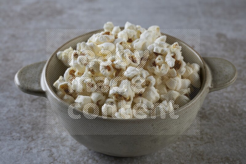popcorn in a off-white handheld ceramic bowl on a grey textured countertop