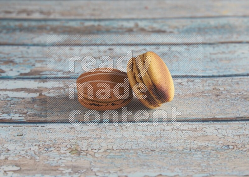 45º Shot of of two assorted Brown Irish Cream, and Yellow Crème Brulée macarons on light blue background
