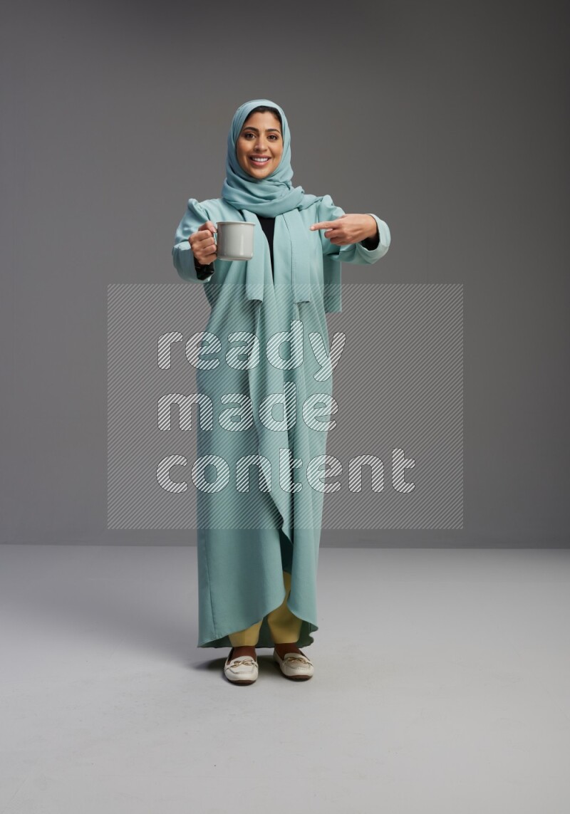 Saudi Woman wearing Abaya standing  holding a mug on Gray background