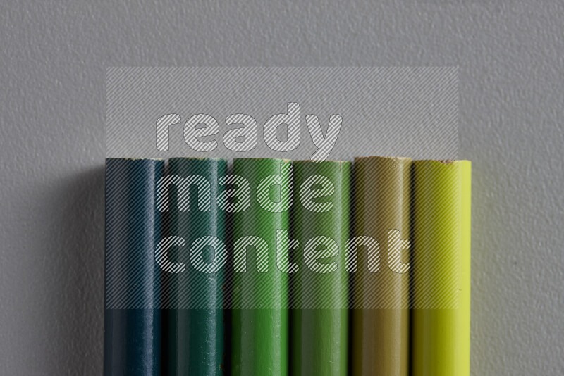 A collection of colored pencils arranged showcasing a gradient of green hues on grey background