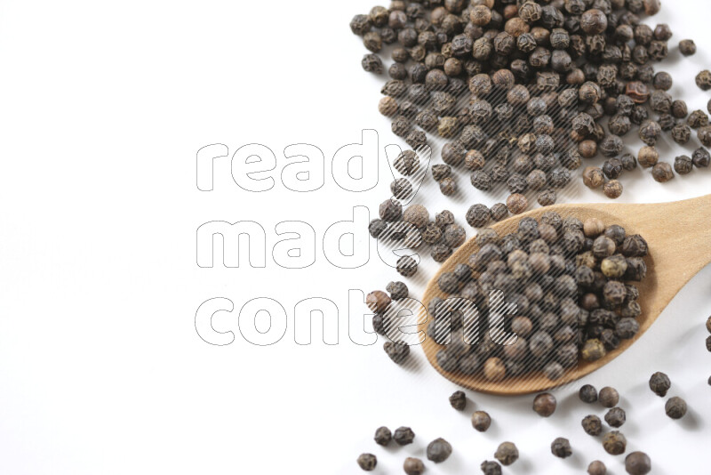 Black pepper beads with wooden spoon on white background