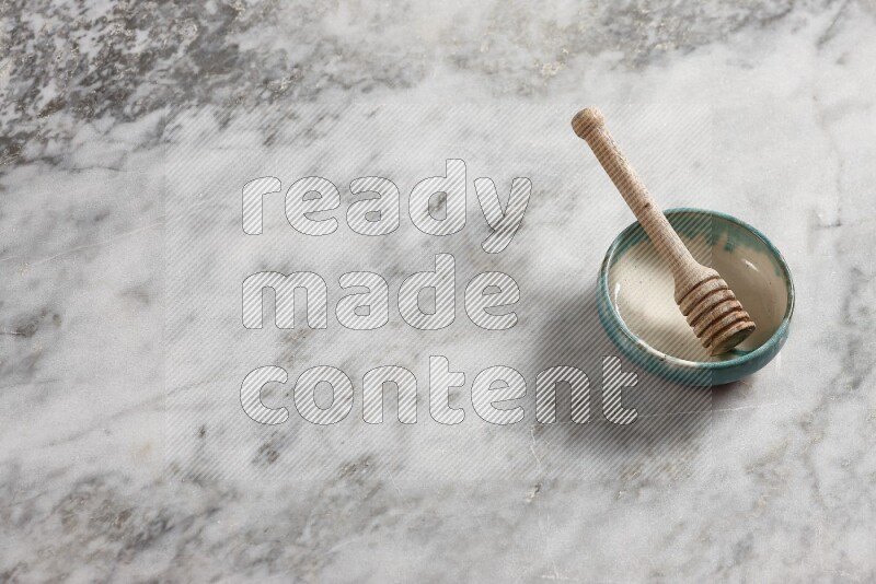 Multicolored pottery bowl with wooden honey dipper in it on grey marble background
