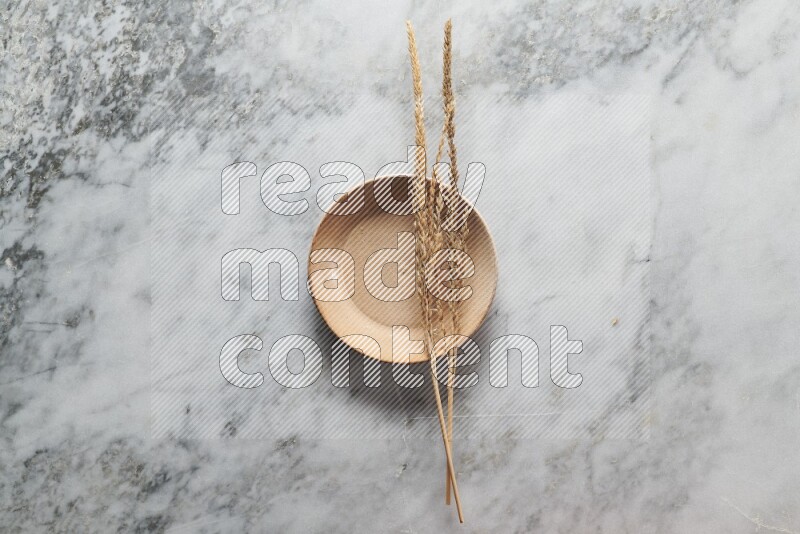 Wheat stalks on beige pottery plate on grey marble background