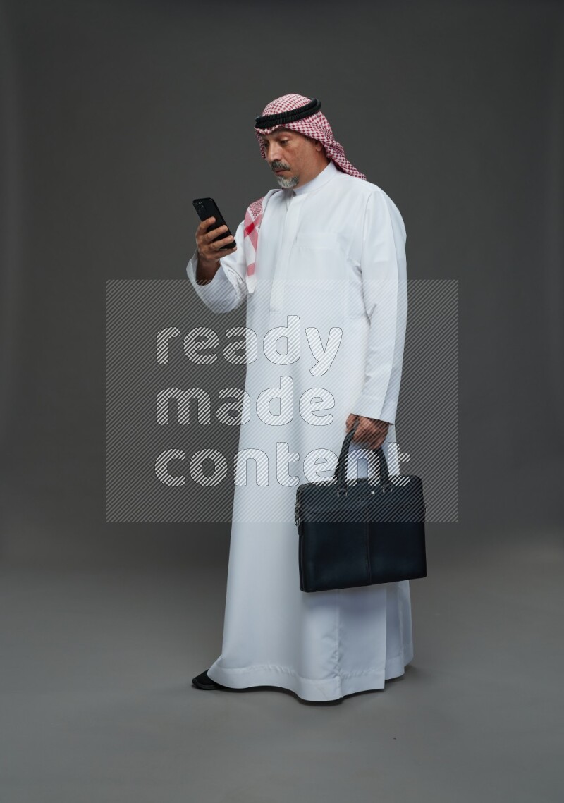 Saudi man with shomag Standing holding bag and phone on gray background