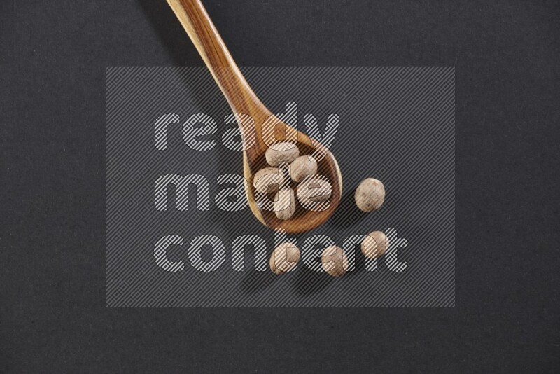 A wooden ladle full of whole nutmeg seeds on a black flooring