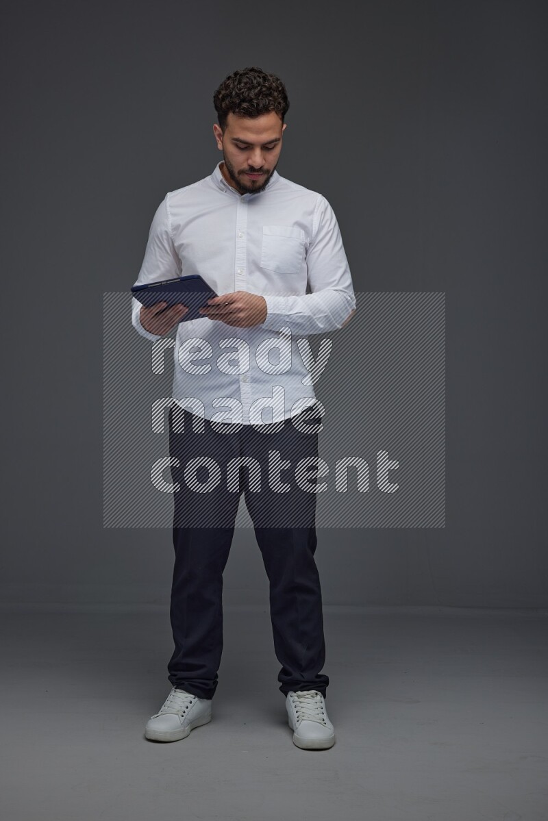 A man wearing smart casual standing and using his tablet eye level on a gray background