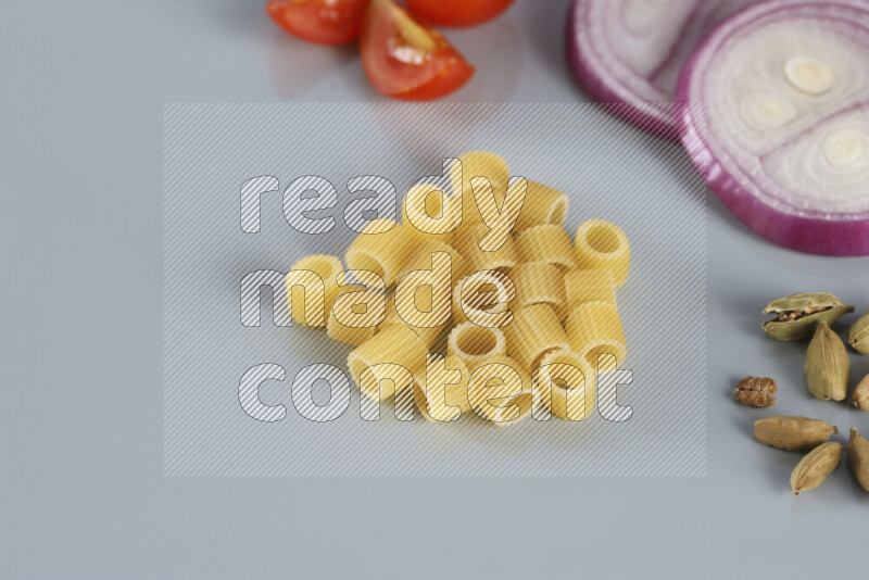 Raw pasta with different ingredients such as cherry tomatoes, garlic, onions, red chilis, black pepper, white pepper, bay laurel leaves, rosemary, cardamom and mushrooms on light blue background