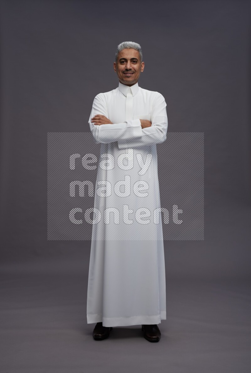 Saudi man wearing thob standing with crossed arms on gray background