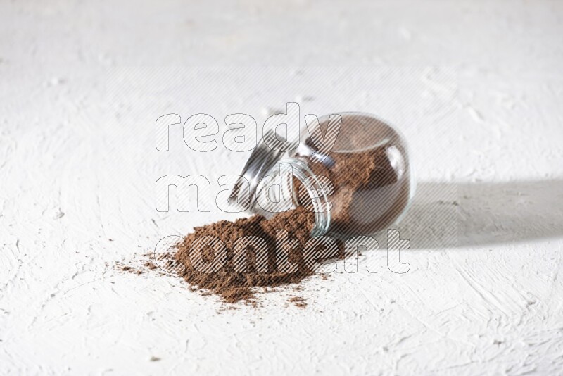 A flipped glass spice jar full of cloves powder and powder came out of it on textured white flooring