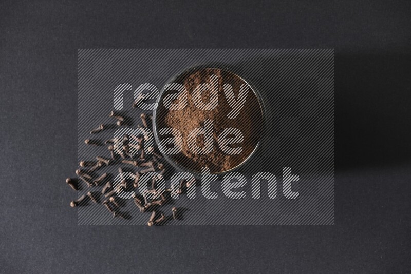 وعاء فخاري أسود ممتلئ ببودرة القرنفل وحبوب القرنفل على خلفية سوداء