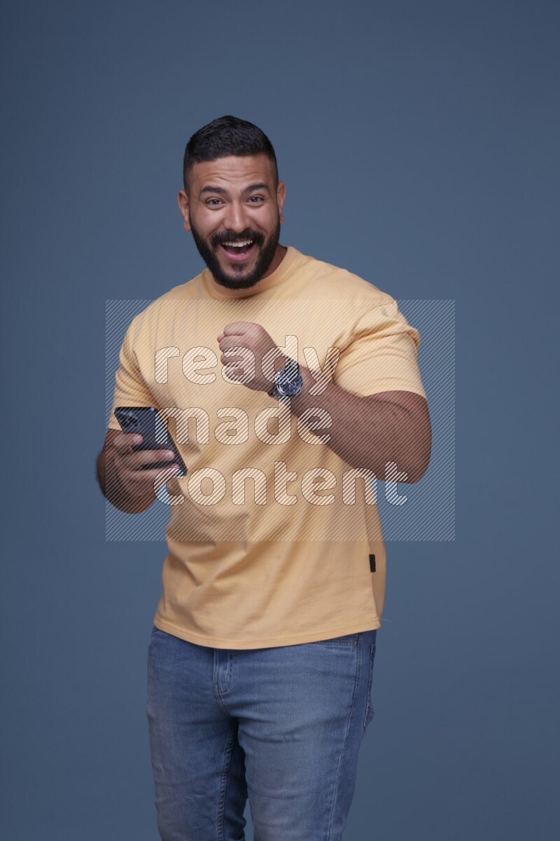 رجل يرتدي قميص اصفر وبنطال جينز ازرق يستخدم جواله