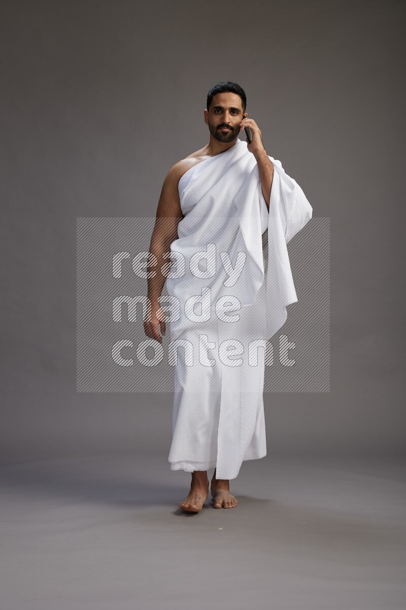 A man wearing Ehram Standing talking on phone on gray background
