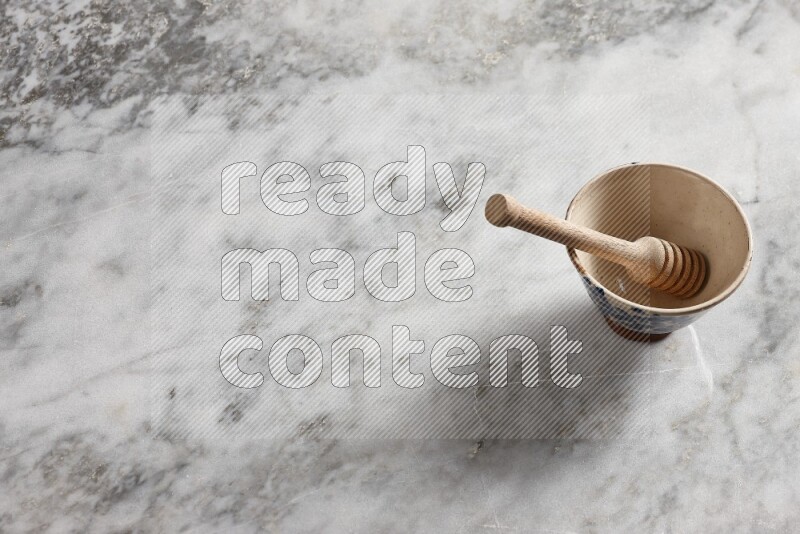 Beige pottery bowl with wooden honey dipper in it on grey marble background