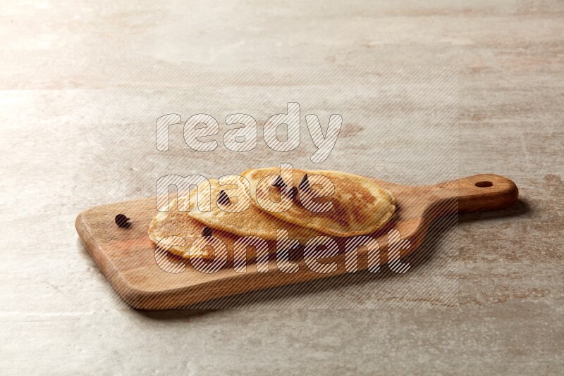 Three stacked chocolate chips pancakes on a wooden board on beige background