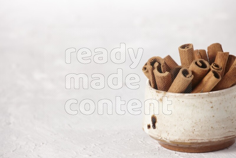 Cinnamon sticks in a beige bowl on a white background