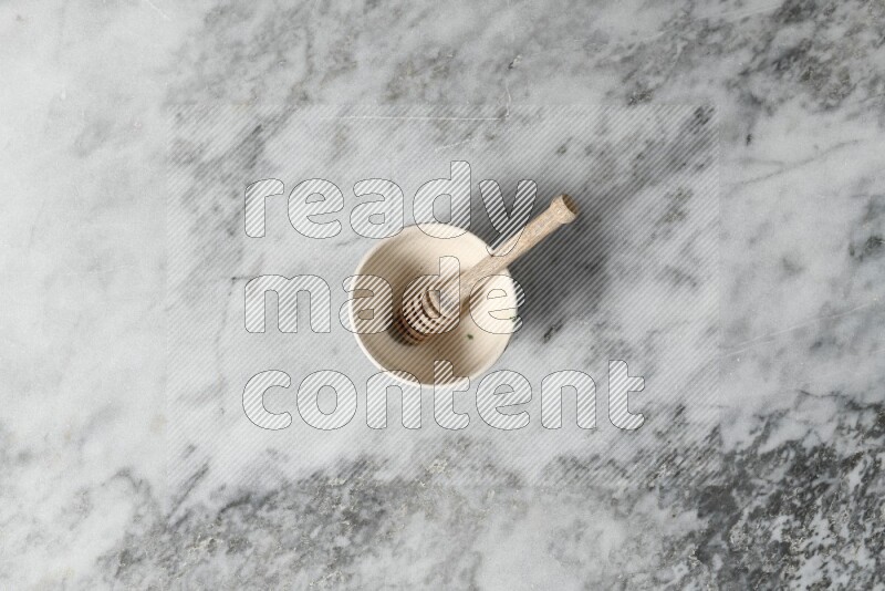 Beige pottery bowl with wooden honey dipper in it on grey marble background