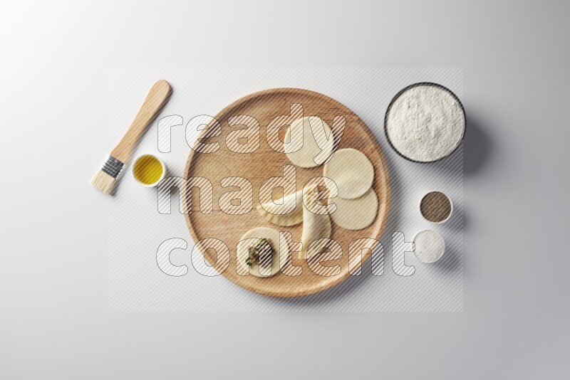 two closed sambosas and one open sambosa filled with meat while flour, salt, black pepper and oil with oil brush aside in a wooden dish on a white background