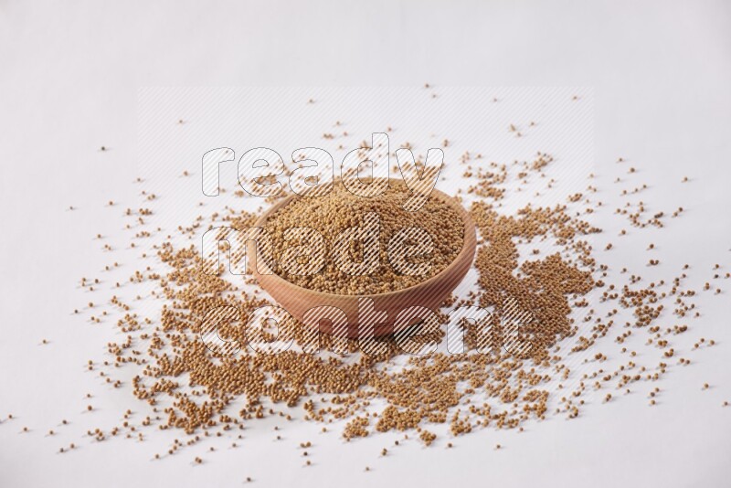 A wooden bowl full of mustard seeds and more seeds spread on a white flooring