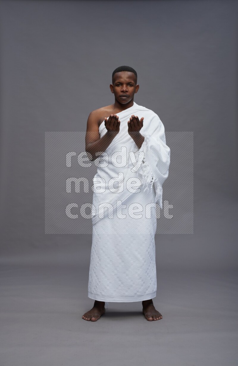 A man wearing Ehram Standing dua'a on gray background