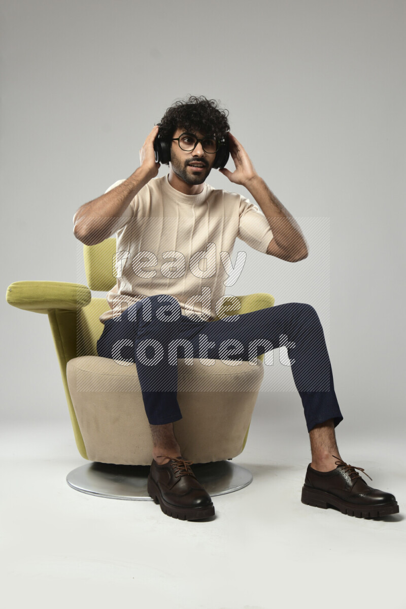 A man wearing casual sitting on a chair putting on headphones on white background