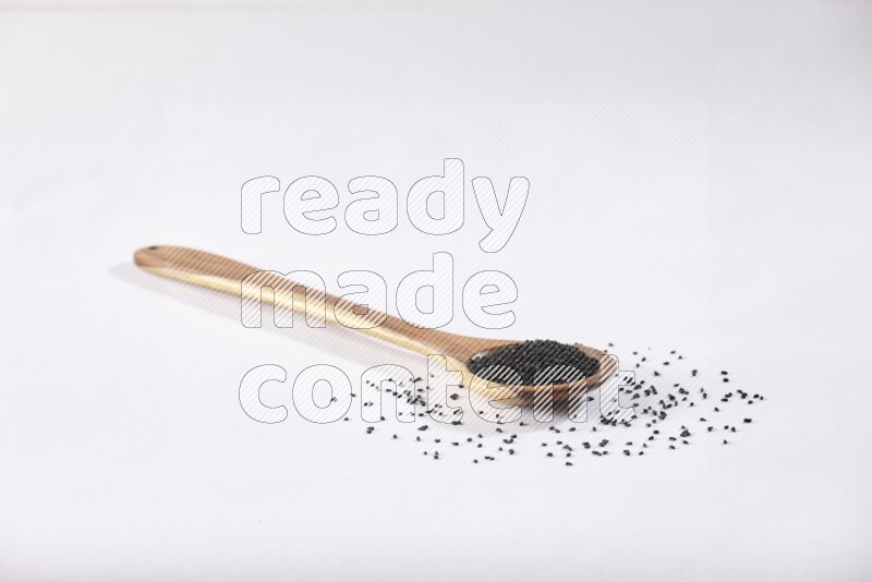 A wooden ladle full of black seeds on a white flooring