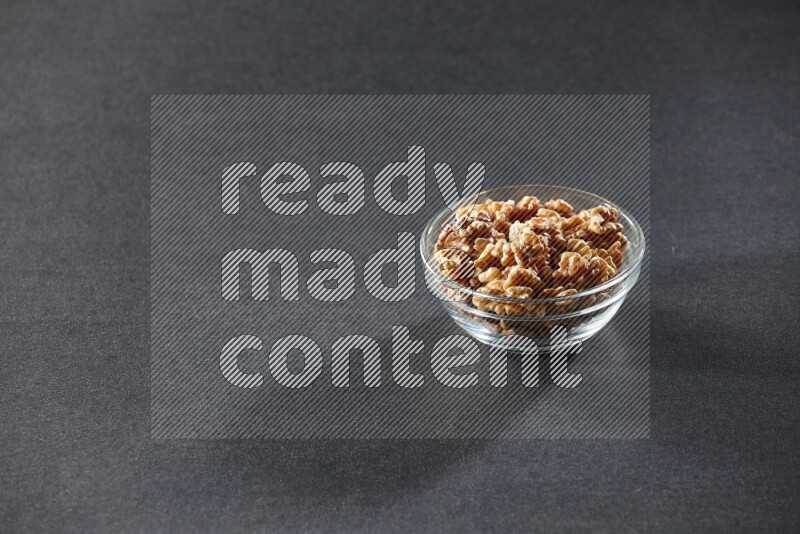 A glass bowl full of peeled walnuts on a black background in different angles
