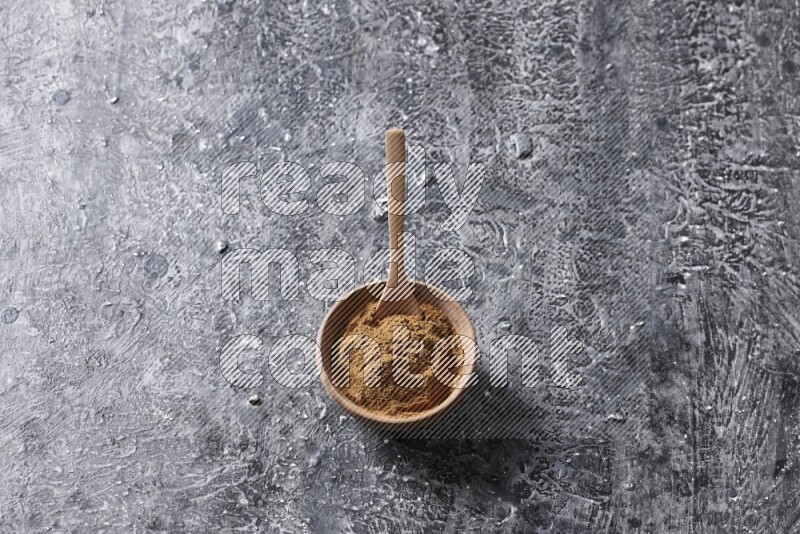 Wooden bowl full of cinnamon powder with a wooden spoon on a textured black background in different angles