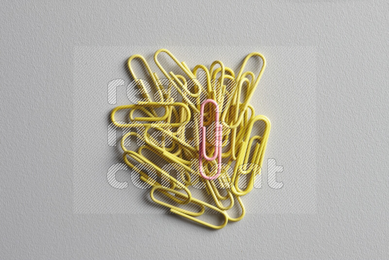 A bunch of yellow paper clips with a different colored paper clip in the center on grey background