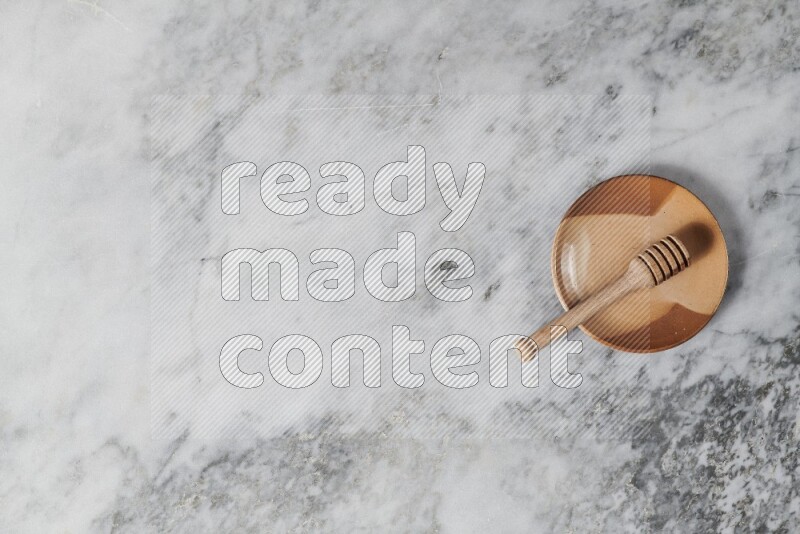Multicolored pottery plate with wooden honey dipper in it on grey marble background