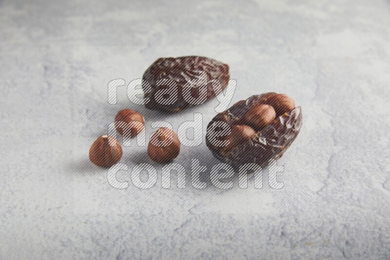 two hazelnuts stuffed madjoul dates on a light grey background