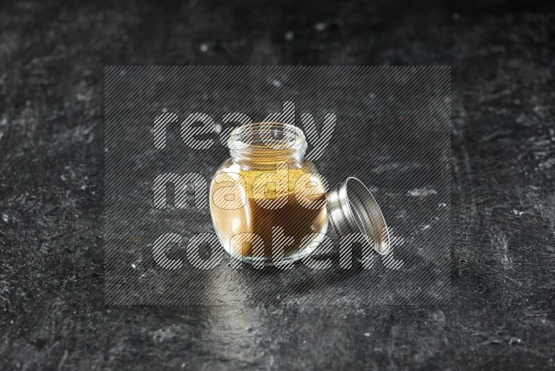 A glass spice jar full of turmeric powder on a textured black flooring