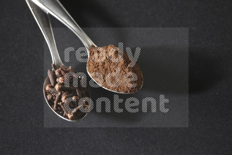 ملعقتان معدنيتان، إحداهما ممتلئة بحبوب القرنفل والأخرى ببودرة القرنفل، على خلفية سوداء