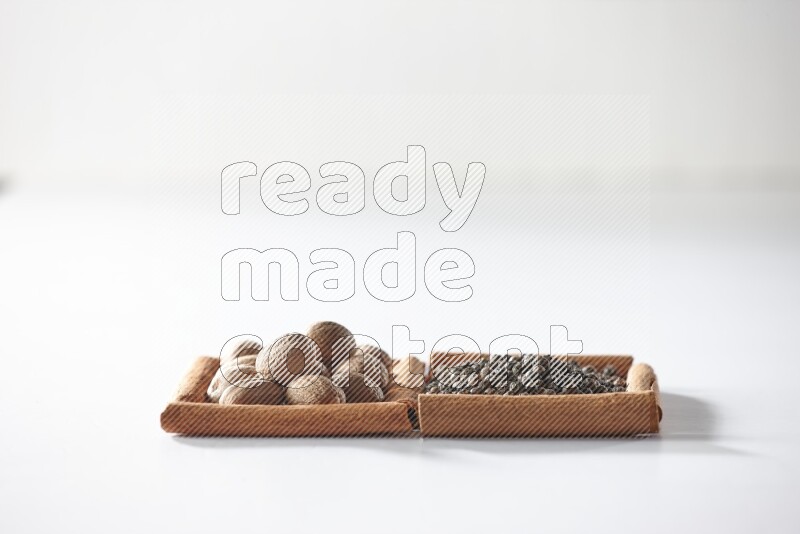 مربعان من أعواد القرفة ممتلئان بحبوب الفلفل الأسود وجوزة الطيب علي خلفية بيضاء