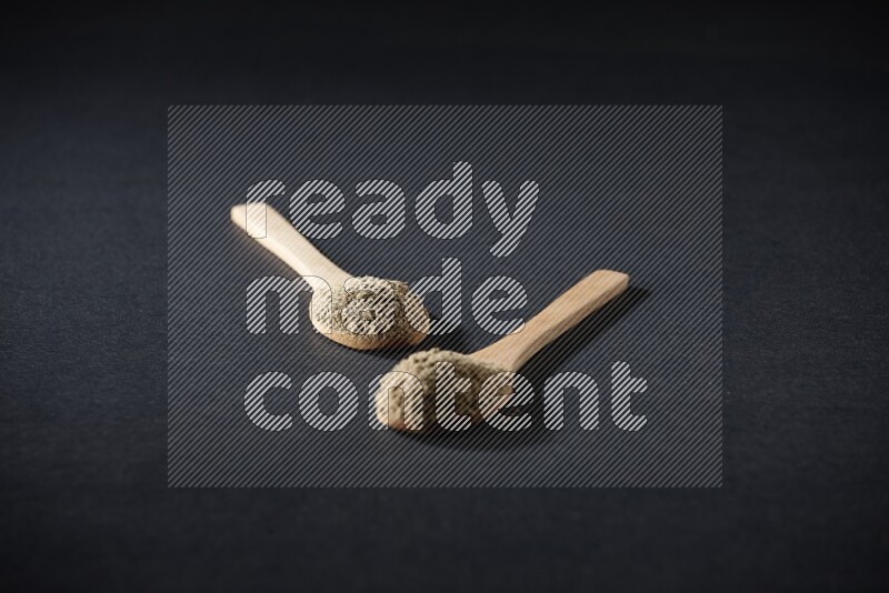 ملعقتان خشبيتان ممتلئتان ببودرة الهيل على خلفية سوداء