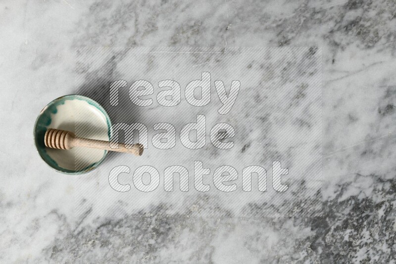 Multicolored pottery bowl with wooden honey dipper in it on grey marble background