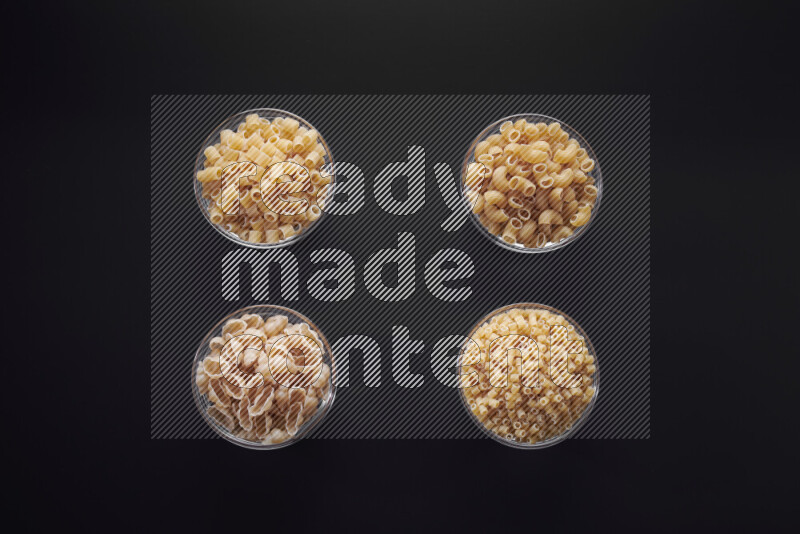 Different pasta types in glass bowls on black background