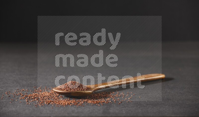 A wooden ladle full of garden cress seeds and seeds spread beside it on a black flooring
