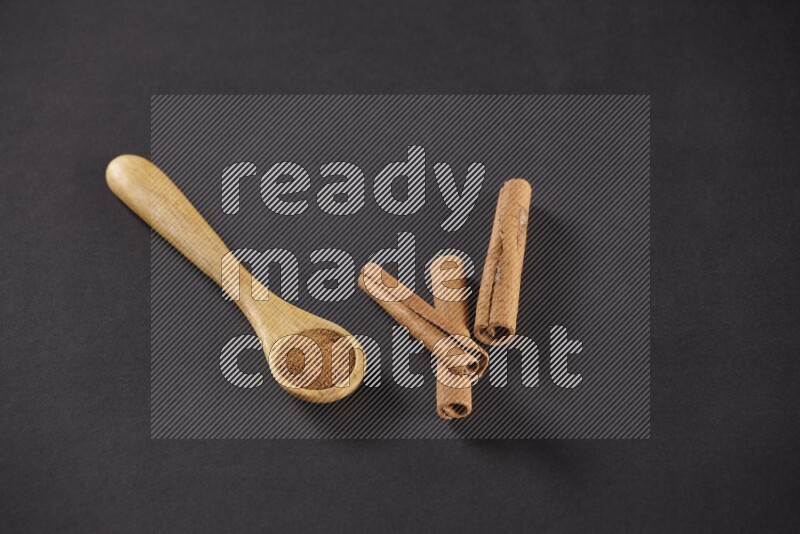 3 Cinnamon sticks stacked beside a wooden spoon full of cinnamon powder on black background in different angles
