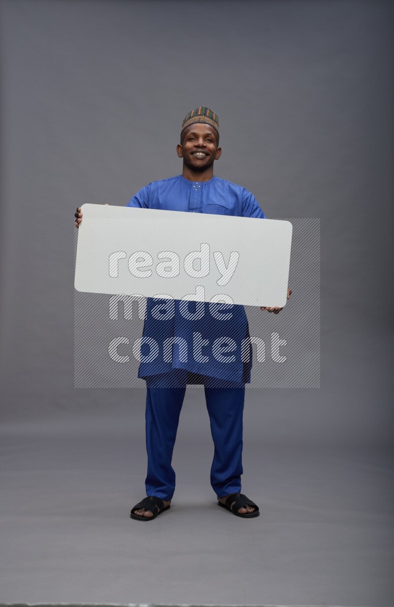 Man wearing Nigerian outfit standing holding board on gray background