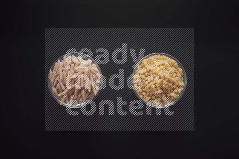 Different pasta types in glass bowls on black background